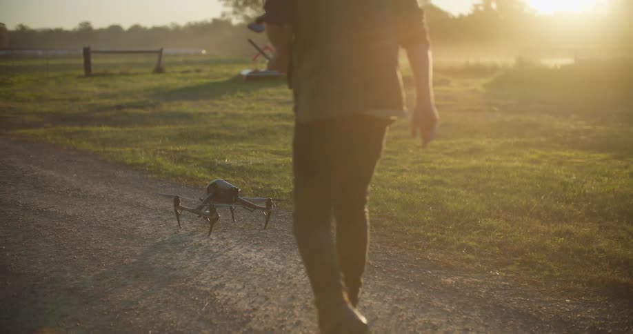 A man uses a radio controller to land a remote controlled drone before retrieving the drone and carrying it away