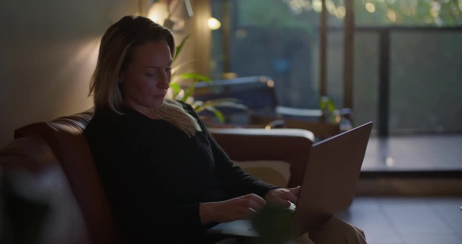 A woman typing on a laptop while sitting on a living room sofa at home