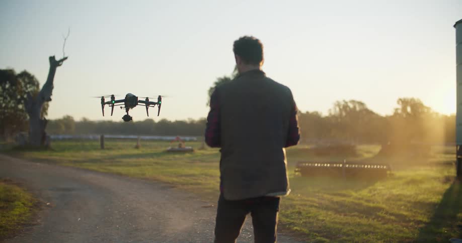 A man is landing a drone in a gravel driveway in a rural area early in the morning