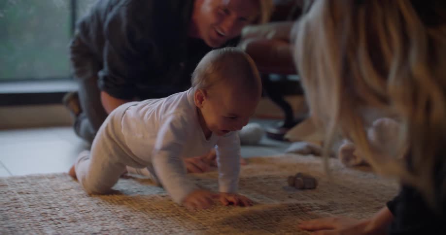 Dad holds baby at the edge of the rug then lets her race crawl over to mommy
