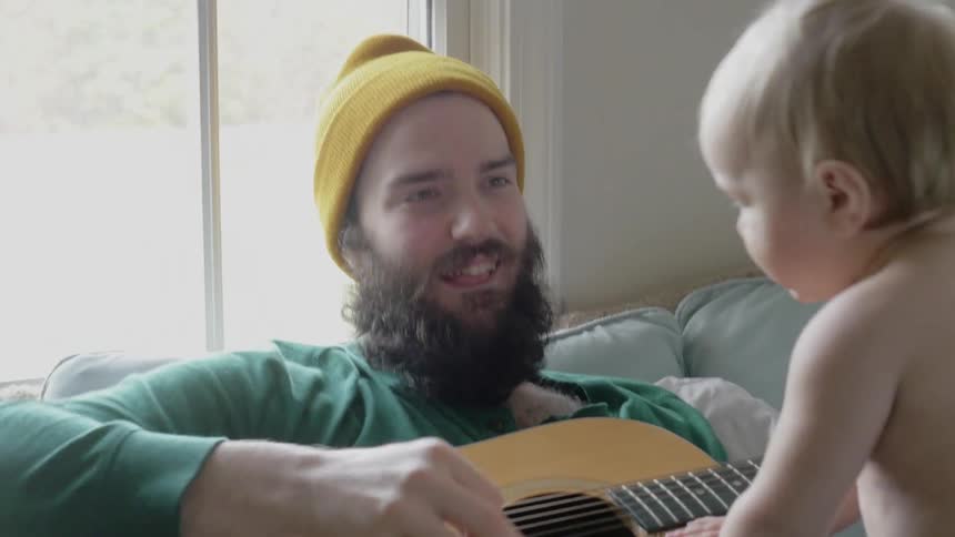 A man plays guitar with a baby on his lap