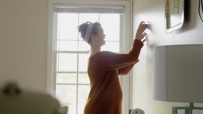 A woman is taping photos to the wall by a window