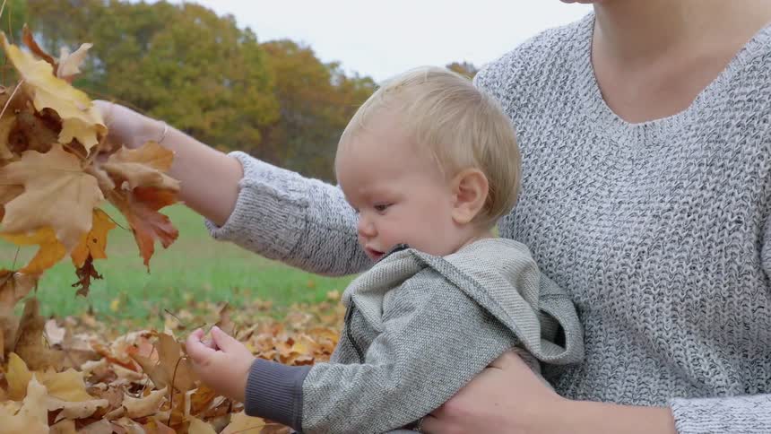 A woman hold her baby in a pile of leaves