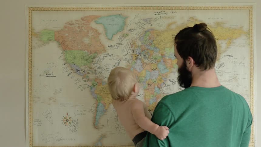 A man holds a baby in front of a world map