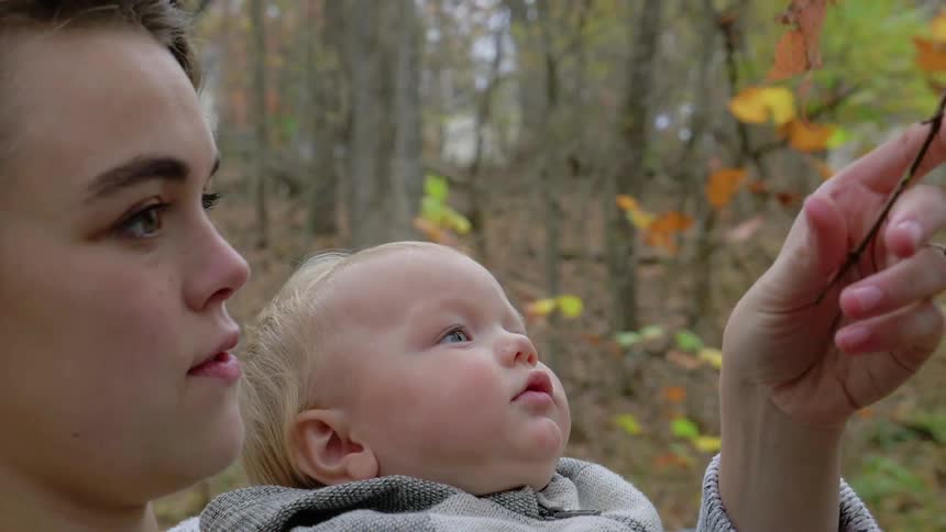 A woman holding a baby points out a branch