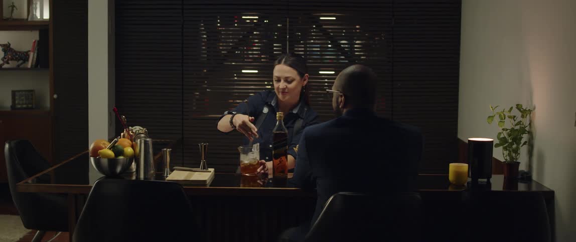 Female bartender preparing a glass of whiskey with a mixing spoon for the man sitting on the bar counter