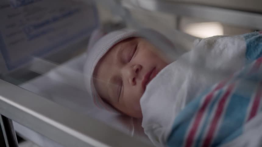 An infant sleeps peacefully in a tiny hospital bed while bundled in blankets