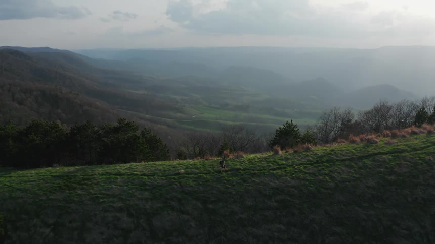 A hiker moves along a trail high in the green lush mountains