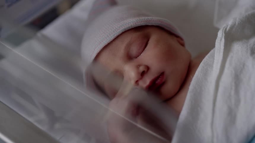 Baby with pink hat and white blanket sleeps in bed
