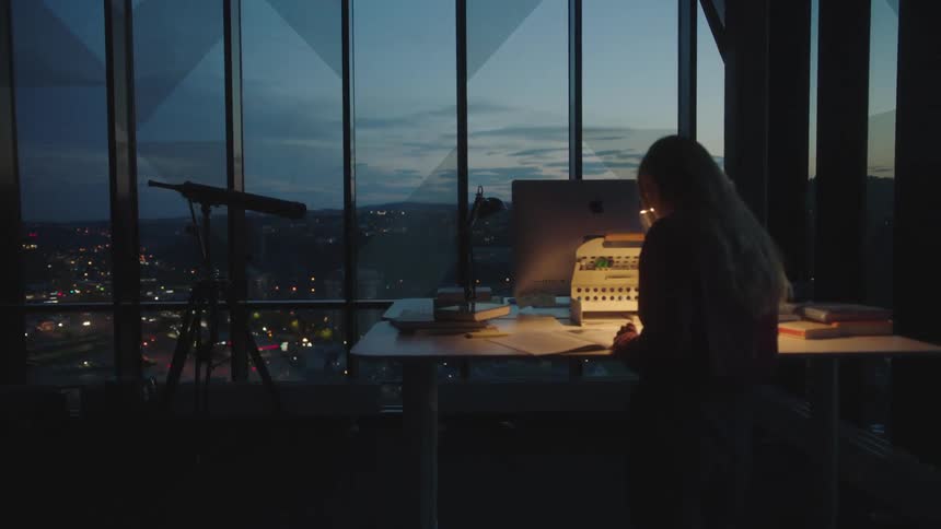 A woman is sitting at her desk near a window at night