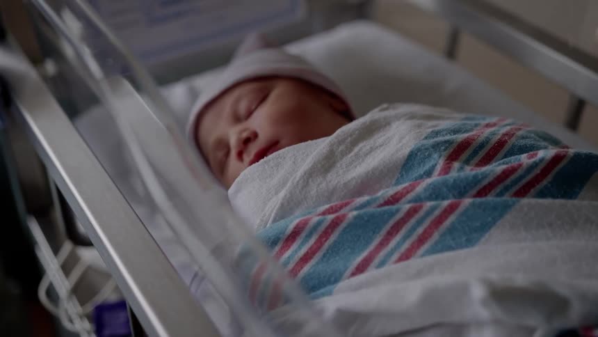 Baby with pink hat and white blanket sleeps in bed