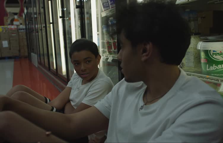 Two boys are sitting in an aisle in a grocery store