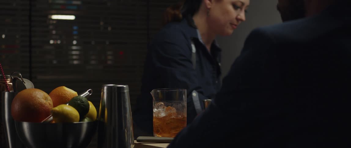 A bartender uses a bar spoon to stir a drink for a customer sitting across from her at a bar