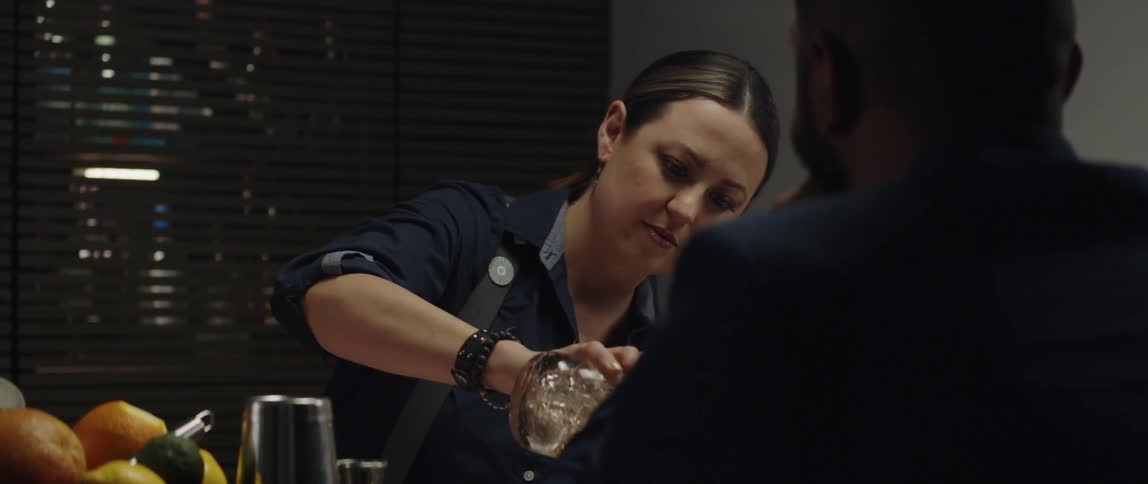 A female bartender pouring a drink for a patron at a bar