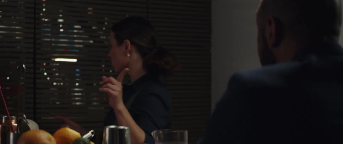 Female bartender talks to client while opening cupboard full of liquor