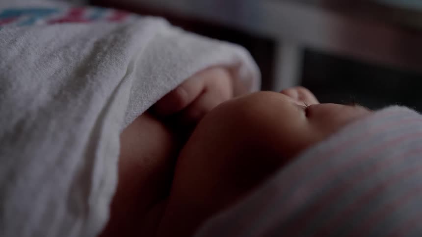 Newborn baby with pink hat and white blanket sleeps in bed