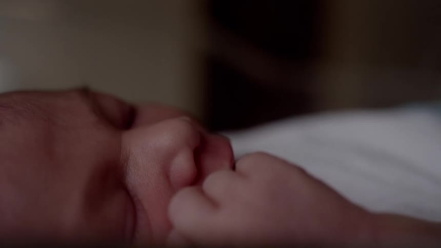 A newborn baby rubs its face and yawns wide with eyes closed
