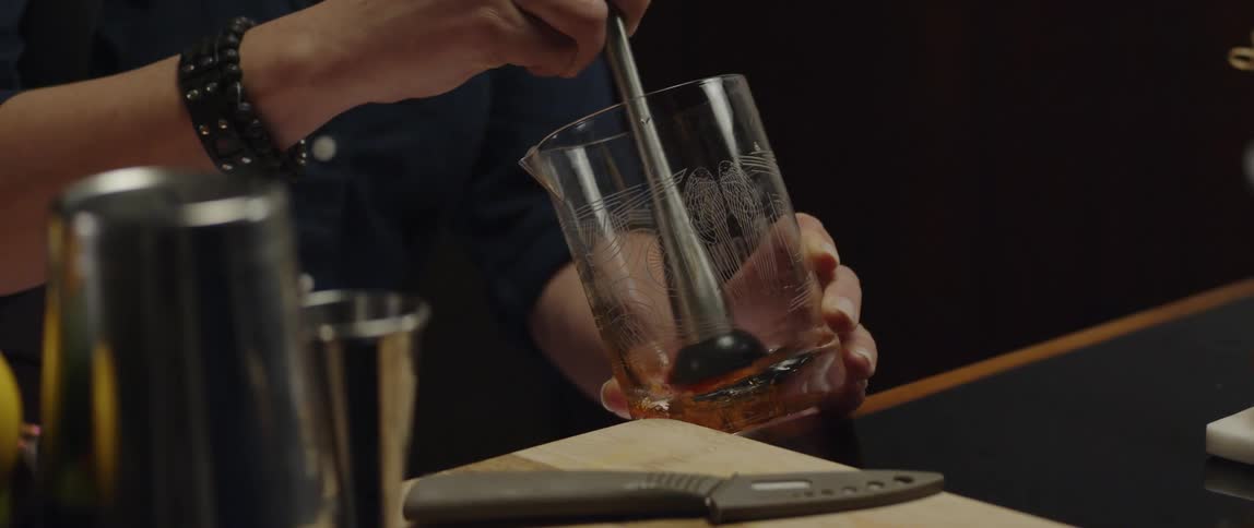 A mans hands are shown stirring a liquid substance at the bottom of a glass