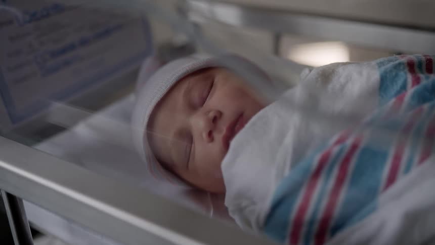 Newborn baby wearing a white cap sleeping on a plastic cradle under blankets