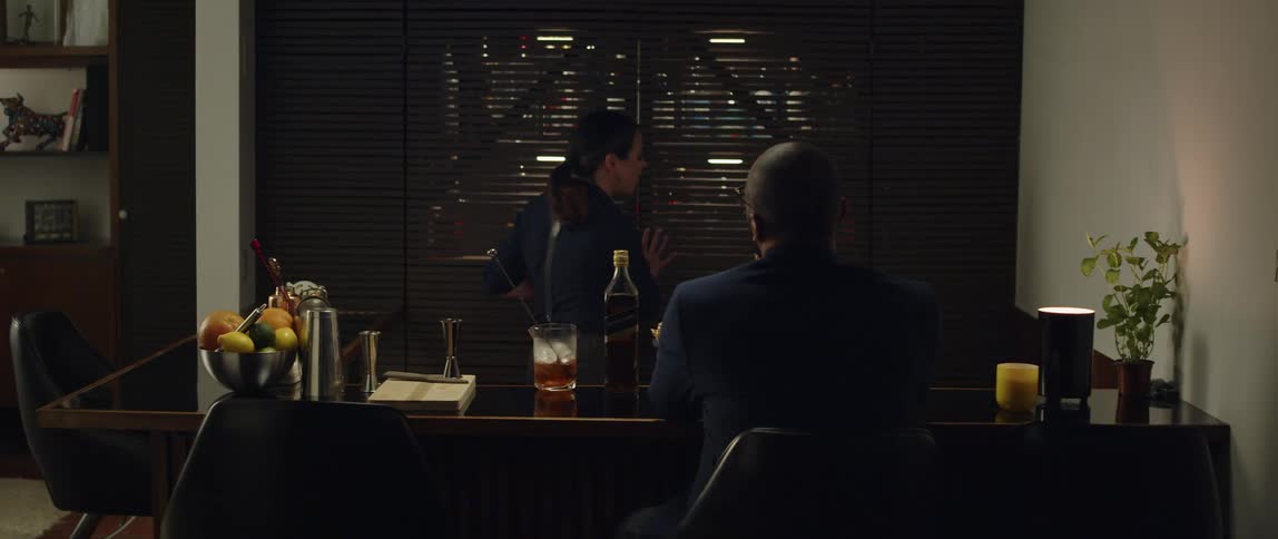 A bartender retrieves a drinking glass from a liquor cabinet and places it before a customer on the bar counter