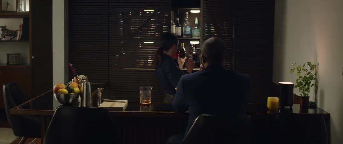 A bartender retrieves a bottle of liquor from a cabinet and prepares to open it for a customer