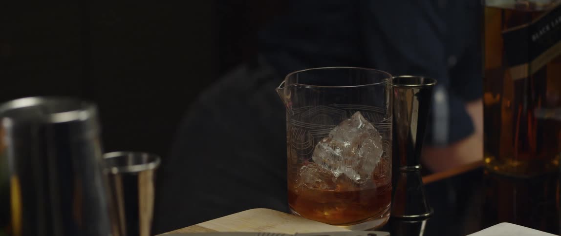 A female bartender adding a scoop of ice to a cocktail