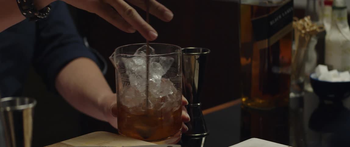 Female bartender preparing a glass of whiskey at the bar counter using a mixing spoon