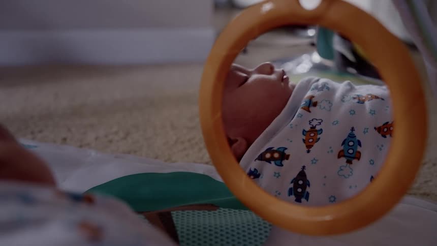 Mirror reflects baby as child sleeps on a blanket on the floor