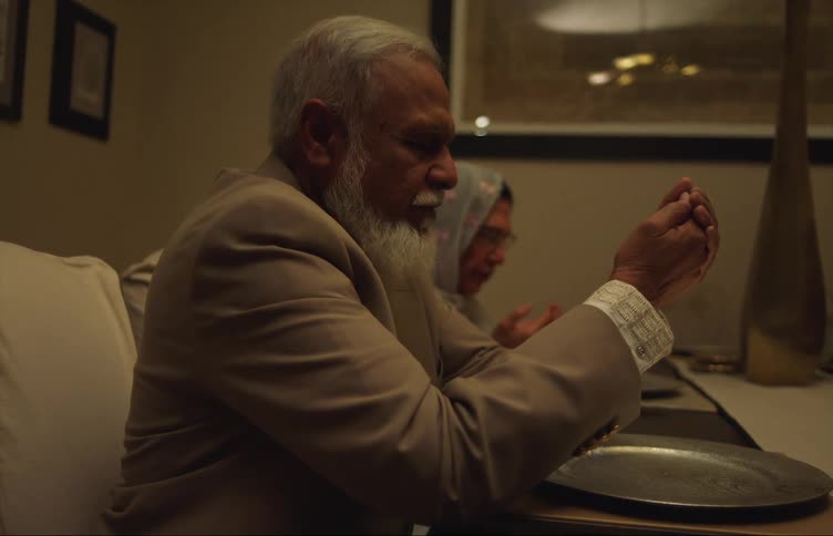 A man and woman are sitting at a dining room table praying over empty plates