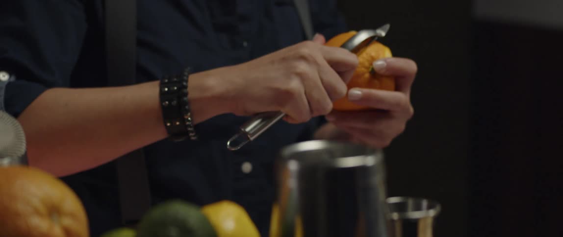 A woman uses a peeler to peel an orange at a restaurant bar