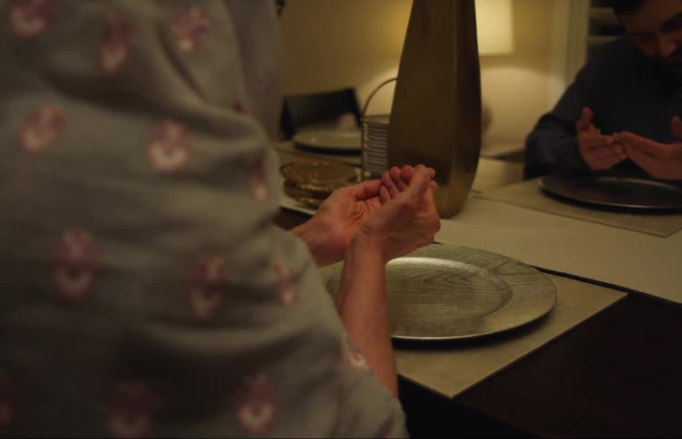 A woman has her hands cupped in front of her as she sits in front of a table praying