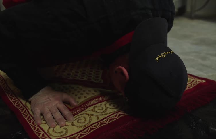 A man touches his forehead to the prayer rug then stands after taking a break at work to pray