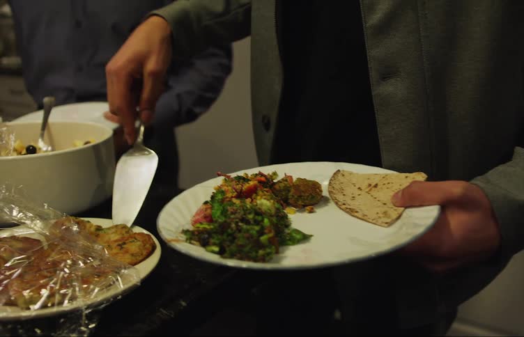 A man puts food on a plate during a potluck style dinner at home
