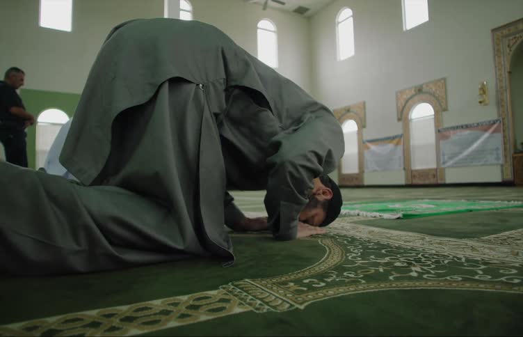 Men are in a mosque praying as they kneel on the floor