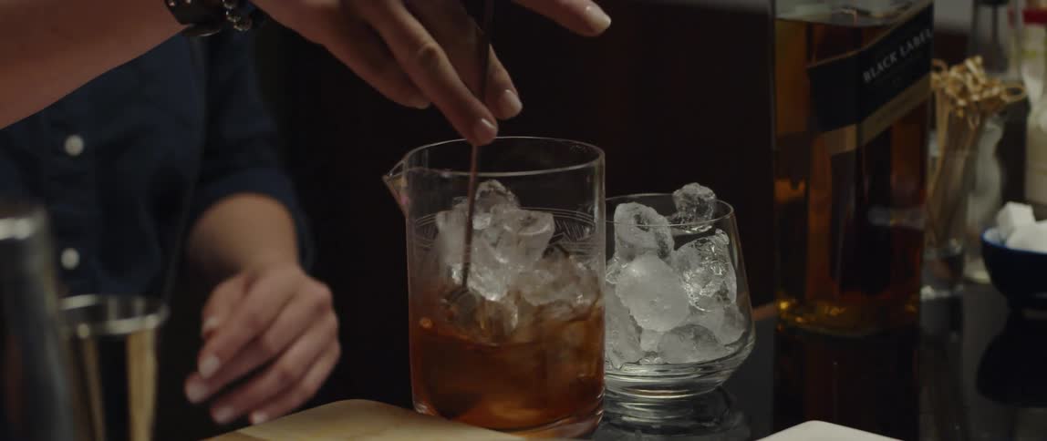 Person stirs alcoholic drink and ice in glass