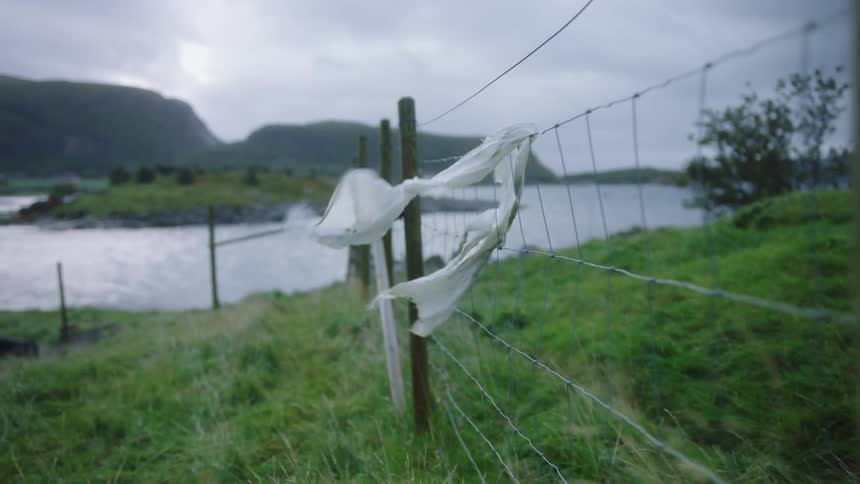 Plastic sheeting flaps on fence leading toward water