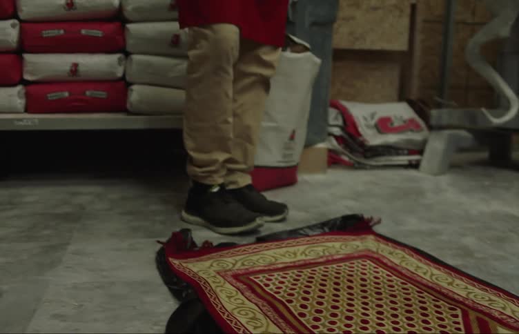 A man lays a rug down then removes his shoes and stands on the rug