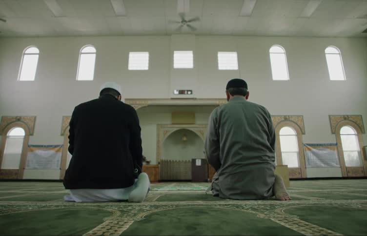 Two muslim men kneeling on the floor of an empty mosque praying