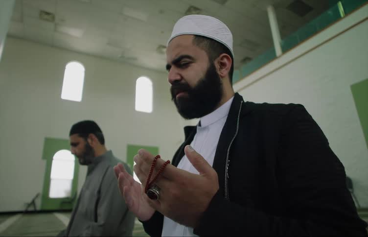 Two muslim men kneeling on the floor and praying at an empty mosque during the day