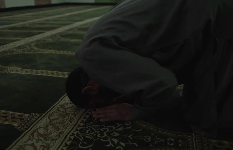 A man in a mosque kneels down to pray on the rug