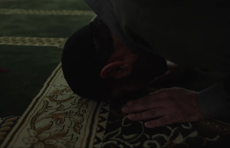 A muslim man kneeling in a mosque places his forehead and hands on the rug praying then rises