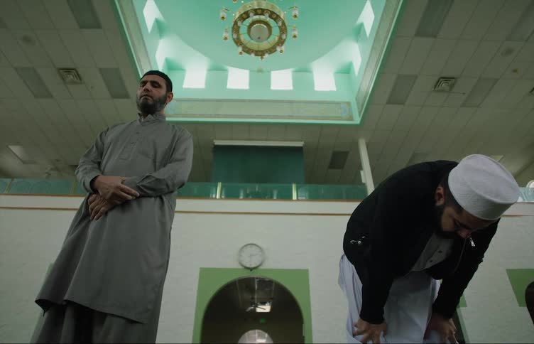 Muslim men with gray shirts pray at the mosque