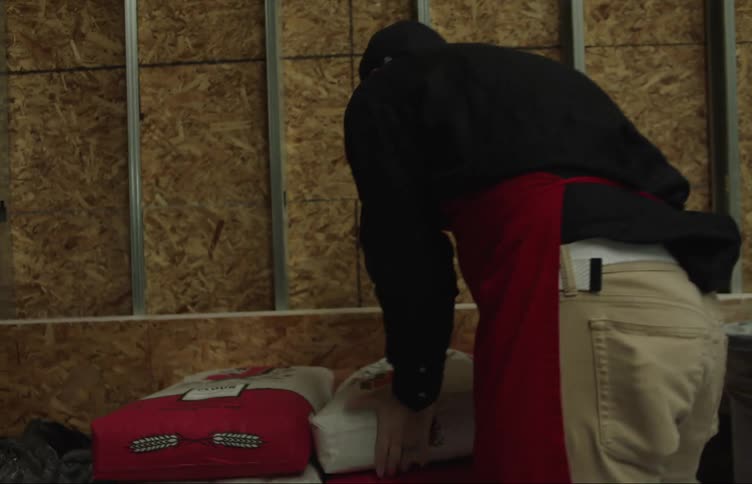 A man moves and stacks large bags of flour in a bakery warehouse