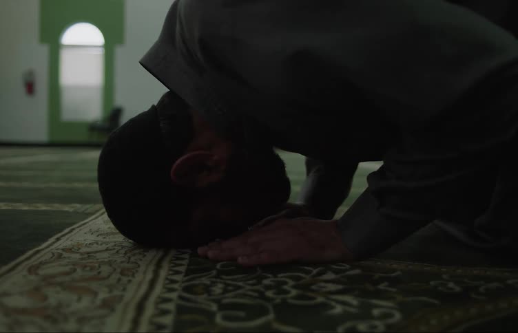 Muslim man with beard and skullcap prays at the mosque