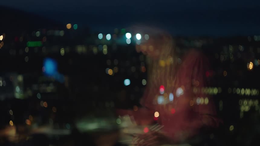 A woman is reflected in her downtown office window working late at night
