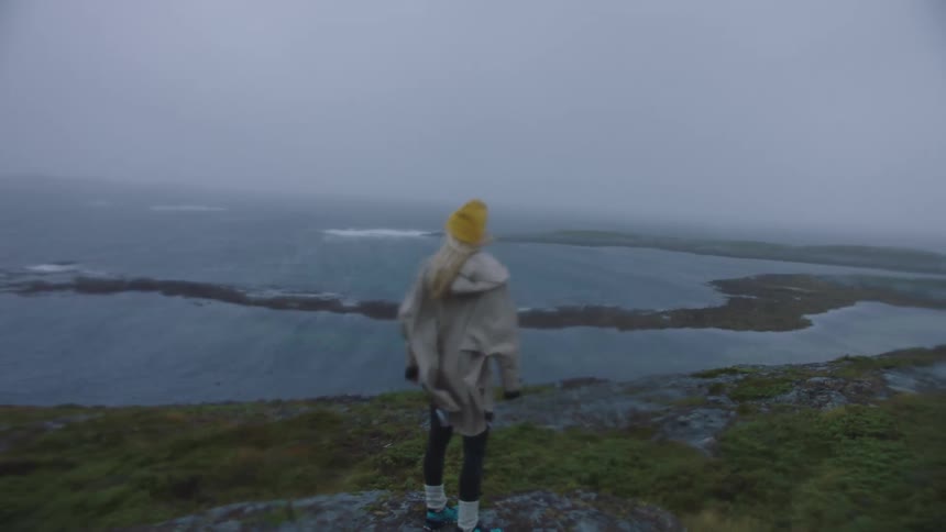 A woman standing on coastal land on a windy foggy day