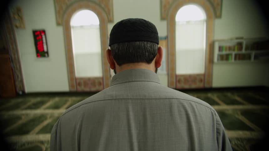 Muslim man with black skull cap prostrates at the mosque