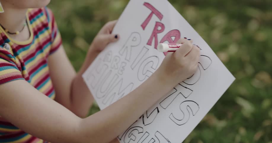 A woman smiles and talks as she sits and colors in letters on a sign