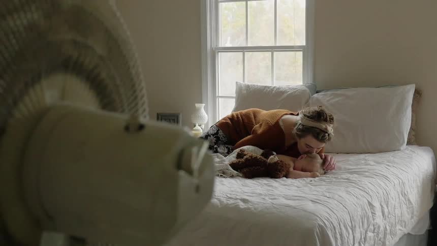 A woman puts a teddy bear near a baby