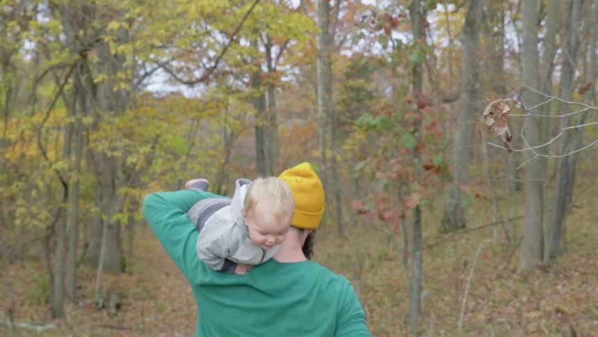 A baby is on the shoulder of a man as he walks in the woods
